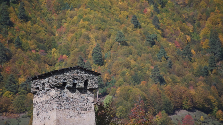 Ancient Svan Tower in Georgia against the mountain slope covered in colorful autumn trees background. Slow motion.