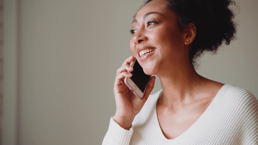 Cheerful African woman talking by phone in the kitchen