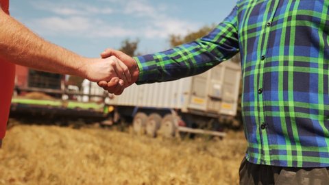 Farmer and agronomist shaking hands standing in a wheat field after agreement. Agriculture business contract concept. Combine harvester driver and rancher negotiate on harvesting season. Handshake