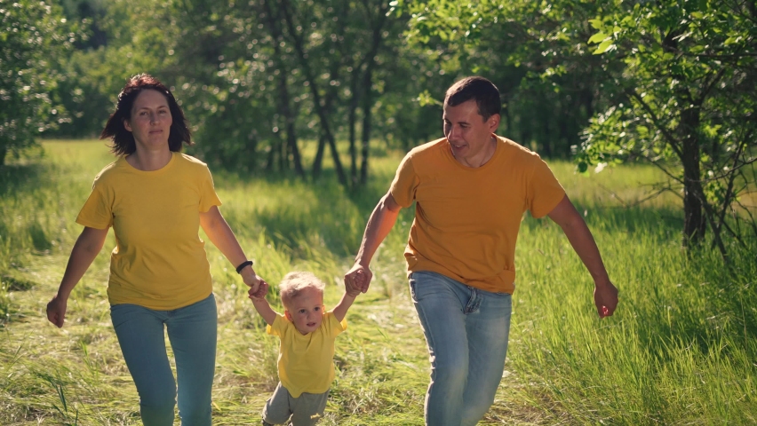 Happy family. Kid with dad and mom plays in the park. Parents with a child run on green grass in a forest park. Family picnic in the park on vacation. Green trees in the sun. People run holding hands