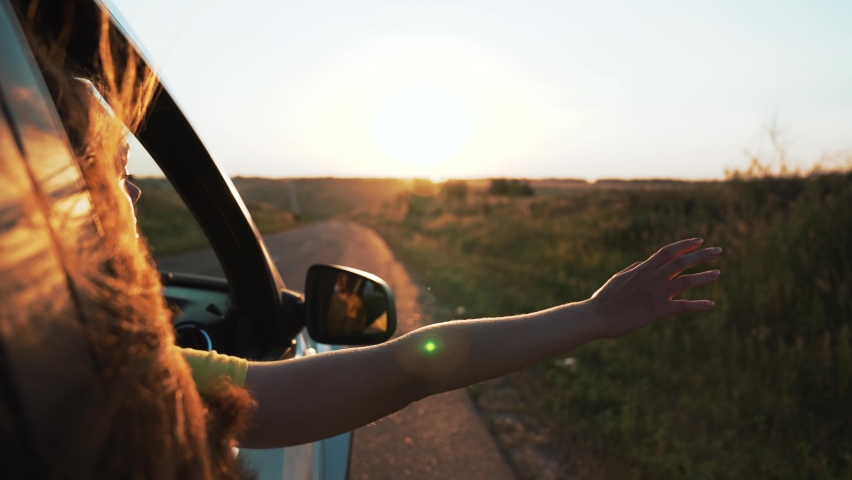 Happy girl in car window. Hair in wind. Girl travels by car. Hand in sun. Windy breeze from car window. Happy girl smiling from car window. Windy breeze in your hair. Hand in the rays of the sun