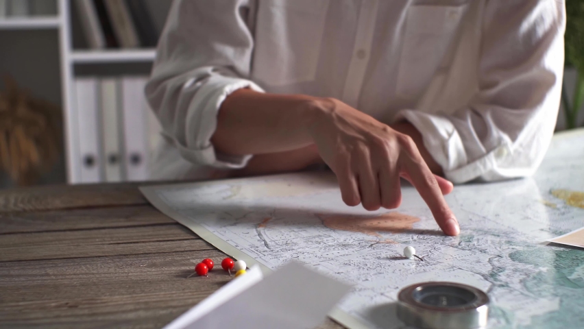 The hand of a young white girl tourist traveler chooses a point on the world map where he would go on his vacation summer adventure travel and vacation world map compass
