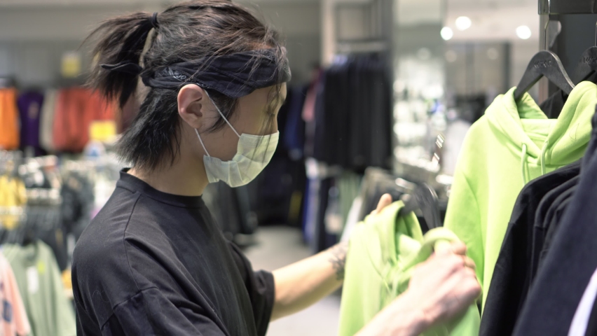 Young Asian man wearing a medical mask in a clothing store. A teenager chooses clothes in a supermarket