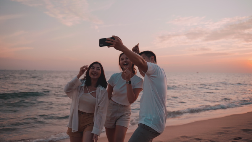 Group of happy Asian friends woman and man using smartphone to take a photo and video together on beach with sunset during summer vacation. Young male and friend taking selfie by cellphone on seaside. - Powered by Shutterstock - Get 15% off with code: PIKWIZARD15