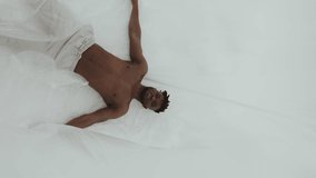 A young black man is in a white room covered in plastic wrap. Vertical video