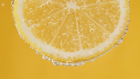 Lemon slice in carbonated water on yellow background, fizzy summer drink, making cocktail of citrus fruits, cold lemonade, ripe sliced fruit. 