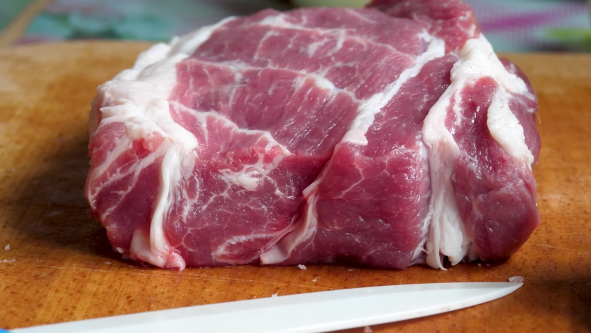 Raw pork meat on chopping board. juicy uncooked organic food for barbecue or BBQ. Culinary name for meat of domestic pig. Most commonly consumed meat worldwide. White kitchen knife  Royalty-Free Stock Footage #1091232659