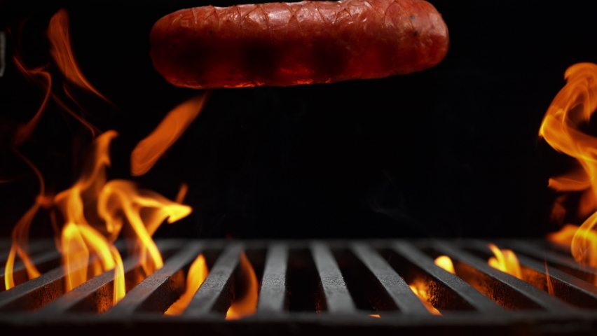 Raw Sausage Falling onto the Grill Grate Flaming in Slow Motion - BBQ on Black Background