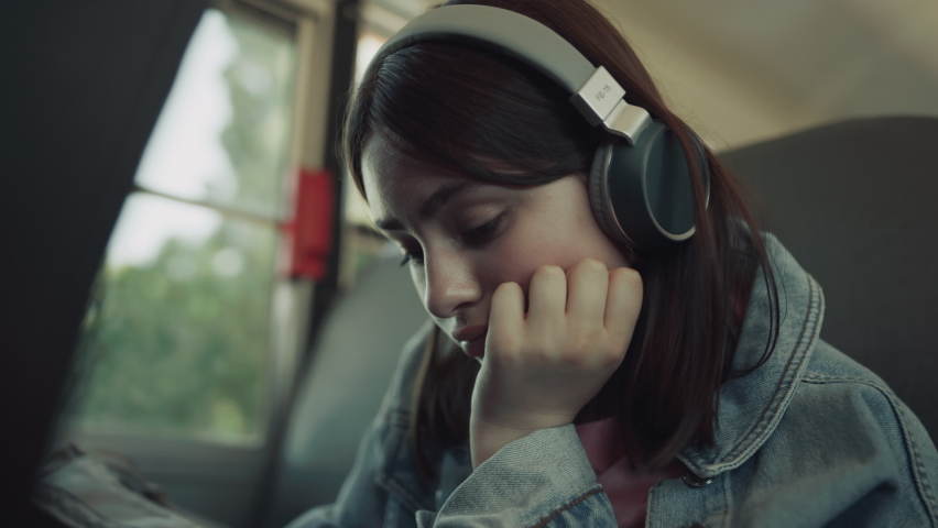 Closeup upset girl sitting schoolbus alone with headphones waiting for ride. Lonely thoughtful teen look down lean on hand. Sad teenager listen music in bus going home. Loneliness in school concept. Royalty-Free Stock Footage #1091248091