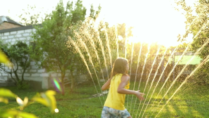 Happy kid girl playing with garden sprinkler run and jump, summer outdoor water fun in the backyard at home, splash on sunny day. Royalty-Free Stock Footage #1091249107