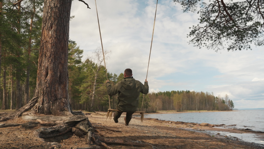 A man in the forest swinging on a swing. Rope swing on a forest lake.