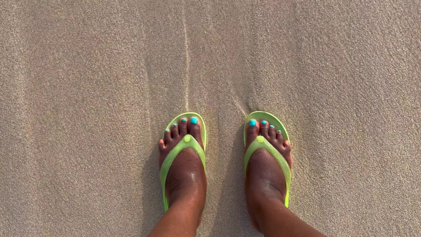 An overhead view of an unrecognizable Black person in sandals standing on a beach with the ocean washing over their feet Royalty-Free Stock Footage #1091252697