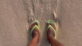 An overhead view of an unrecognizable Black person in sandals standing on a beach with the ocean washing over their feet - Powered by Shutterstock - Get 15% off with code: PIKWIZARD15