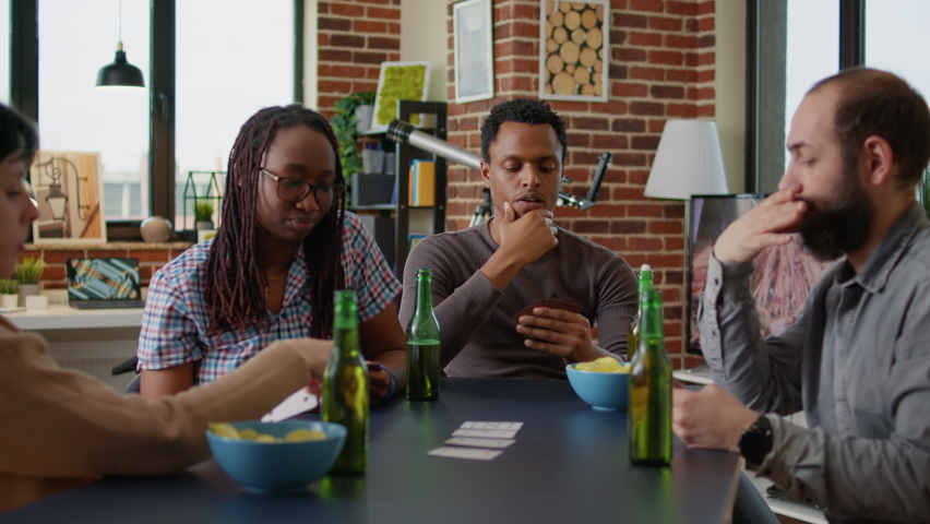 Portrait of african american man thinking about strategy play at card games with friends, having fun in living room. Young adult enjoying board game play with tactics, drinking beer with people. Royalty-Free Stock Footage #1091256063
