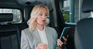 Portrait of serious caucasian business lady talking on smartphone in modern car. Attractive businesswoman in formal clothes talking on mobile phone in business car
