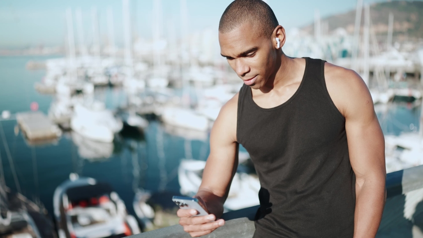 Bald happy sportsman wearing black T-shirt typing on phone outdoors in the morning