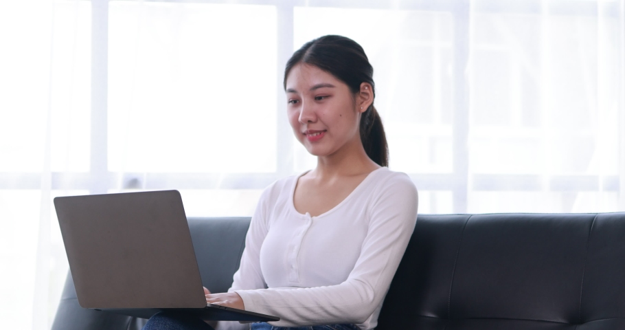 Happy millennial hispanic teen girl checking social media holding laptop at home. Smiling young asian woman using mobile phone app playing game, shopping online, ordering delivery relax on desk.
 Royalty-Free Stock Footage #1091262951