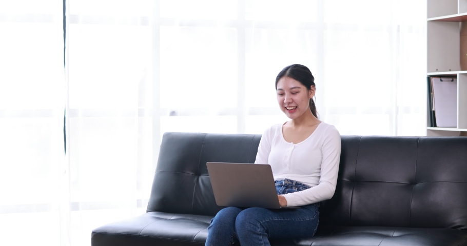 Happy millennial hispanic teen girl checking social media holding laptop at home. Smiling young asian woman using mobile phone app playing game, shopping online, ordering delivery relax on desk.
 Royalty-Free Stock Footage #1091262953
