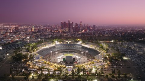 Epic downtown view on pink cinematic sunset. Drone flying above Dodgers stadium illuminated at night on cinematic evening. Skyscraper buildings, Sport game at Dodgers Stadium Los Angeles USA June 2022