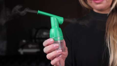 woman holding an oxygen inhaler in her hand with steam coming out of it. the nebulizer works