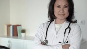 Close up portrait of beautiful asian female professional doctor in lab coat healthcare assistant standing in modern hospital and smiling to camera in good mood. 4k footage