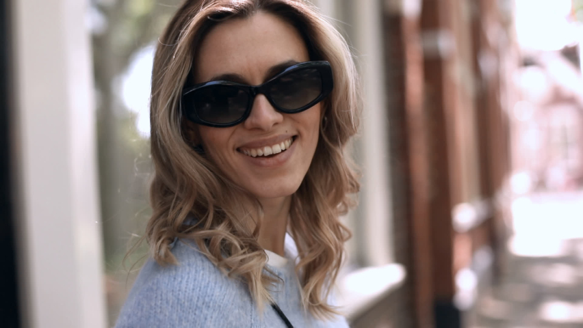Woman with flying hair posing walking in the street. Back view of trendy modern female in casual outfit spinning around on street with blond hair flying in wind. Cheerful and happy girl. Slow motion.