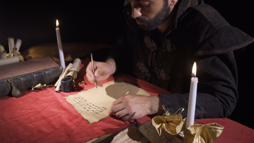 Europe in the Middle Ages.
Medieval man writing letters by candlelight using the English alphabet. Writing with ink.

