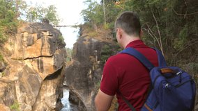 Casual travel blogger shooting video of amazing nature in national park in Thailand. Back view of 30s forest hiker photographer man with backpack make video of canyon for social media on mobile phone