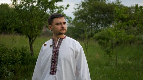 Calm and concentrated caucasian man in traditional embroidered vyshyvanka looking into distance and surveying the horizon. Ukrainian in authentic national shirt scouting the skyline outdoors
