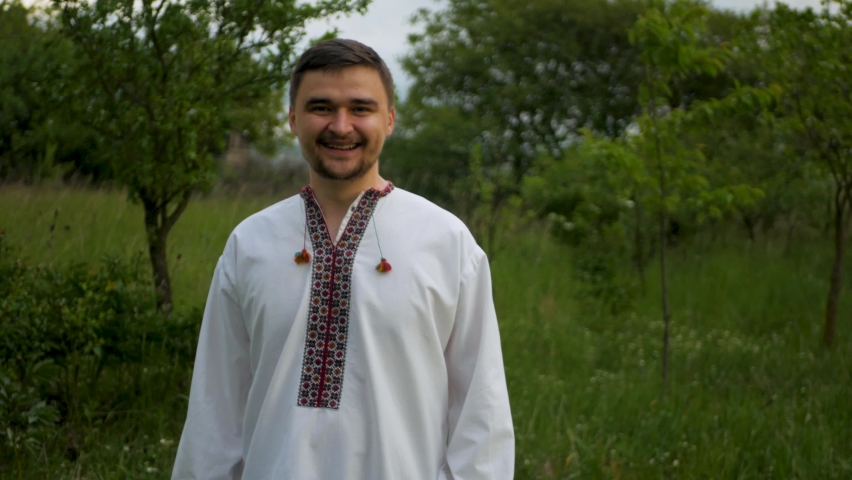 Happy caucasian man in traditional Eastern European embroidered shirt celebrating and cheering. Beaming bearded guy in conventional vyshyvanka rejoicing and clenching fists due to victory and success
