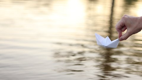 child puts a paper boat into the water. happy family fantasy kid dream concept. child playing with paper boat ship. a child hand launches a boat in a park in a lifestyle pond. High quality 4k footage.