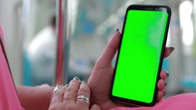 Female hands are holding a smartphone and touching the screen with their fingers. On-screen green rear background.