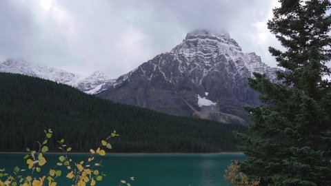 Scenic Cinematographic view of Mountains with snow peaks and pine woods in Banff National Park on a sunny day. Lake with turquoise water.Green autumn forest in the Rocky Mountains in Canada.