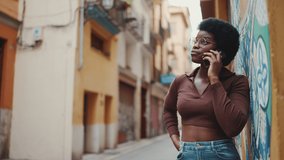 African girl in glasses talking over mobile phone on the street. African American woman looking stylish talking with friend on smartphone outdoors
