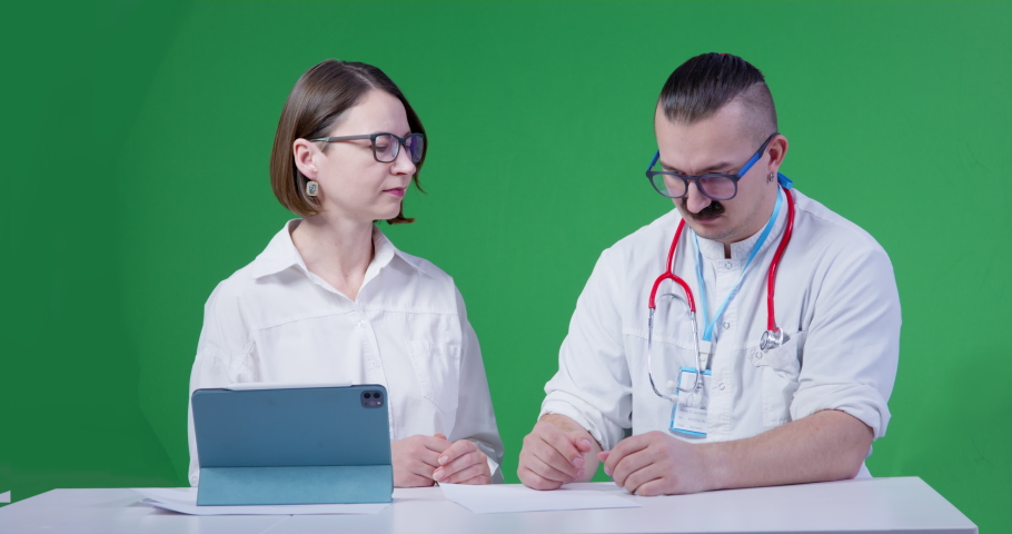 Doctor in uniform and with stethoscope around his neck is sitting at interview or at appointment of therapist, when he suddenly has an attack and starts shaking. Young woman is trying to help him Royalty-Free Stock Footage #1091272317