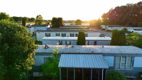 Low drone flyover of mobile homes. Sunburst on lens from sunset in spring. Mobile home park for low income families in USA.