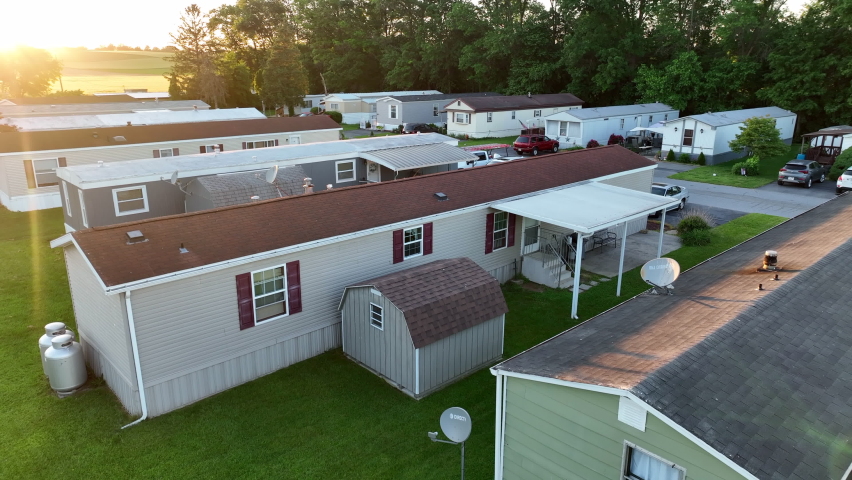 Aerial pull back from mobile home in America. Reveal of beautiful golden hour light over sprawling mobile home park. Low income housing in rural USA.