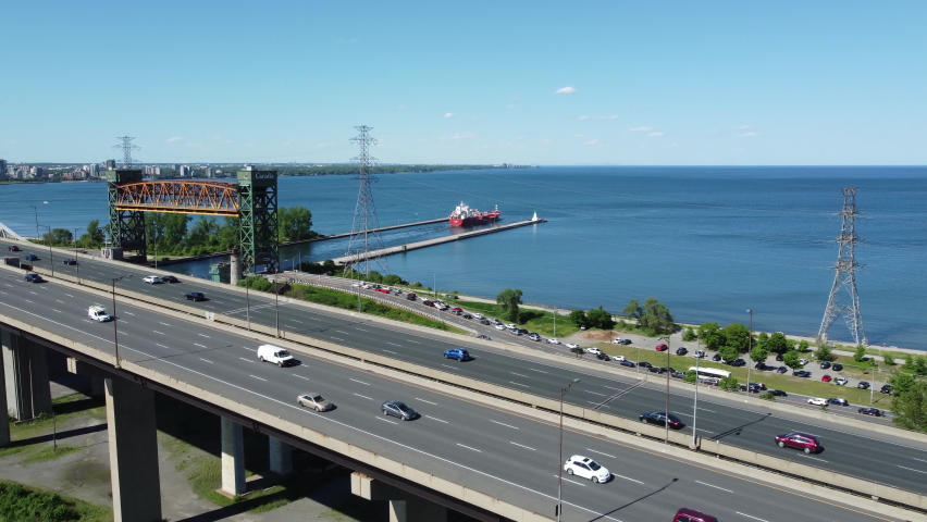 Cars Driving On The Burlington Skyway Crossing The Burlington Bay Canal In Ontario, Canada. Burlington Canal Lift Bridge In Background. aerial drone