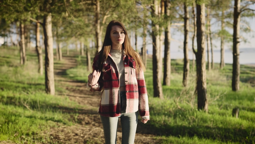 Beautiful young hipster woman in a shirt walking through a picturesque pine forest.