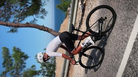 Cyclist with muscular fit body in sportswear and white helmet riding road bicycle, climbing uphill through mountain hill. Vertical video. Recreation sport cycling. Athlete sports workout training