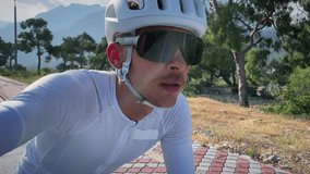 Portrait of professional male cyclist on sport race bicycle. Man athlete in white helmet and cycling jersey riding on bike outdoors and making selfie videos. Active sport. Recreation leisure activity