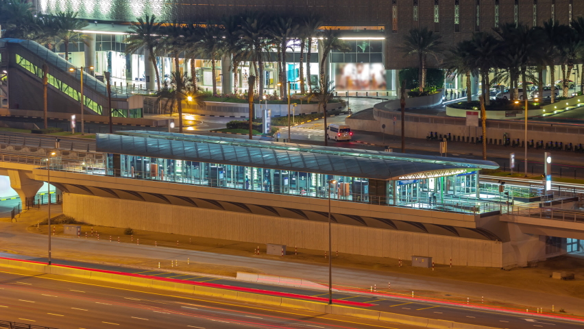 Futuristic building of Dubai tram station and shopping mall behind in Dubai Marina aerial night timelapse. Traffic on Sheikh Zayed road highway, United Arab Emirates