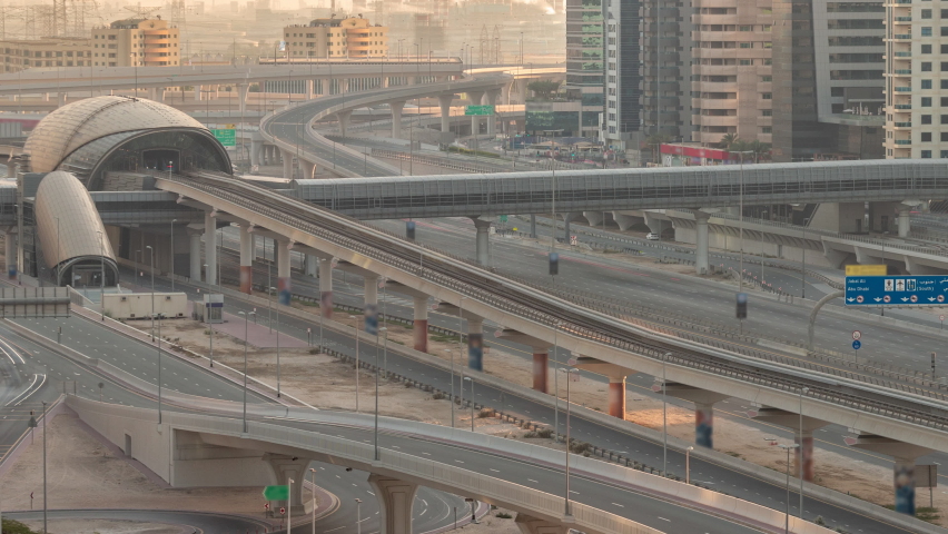 Futuristic building of Dubai metro station and luxury skyscrapers behind in Dubai Marina aerial timelapse. Traffic on Sheikh Zayed road highway with overpass, United Arab Emirates