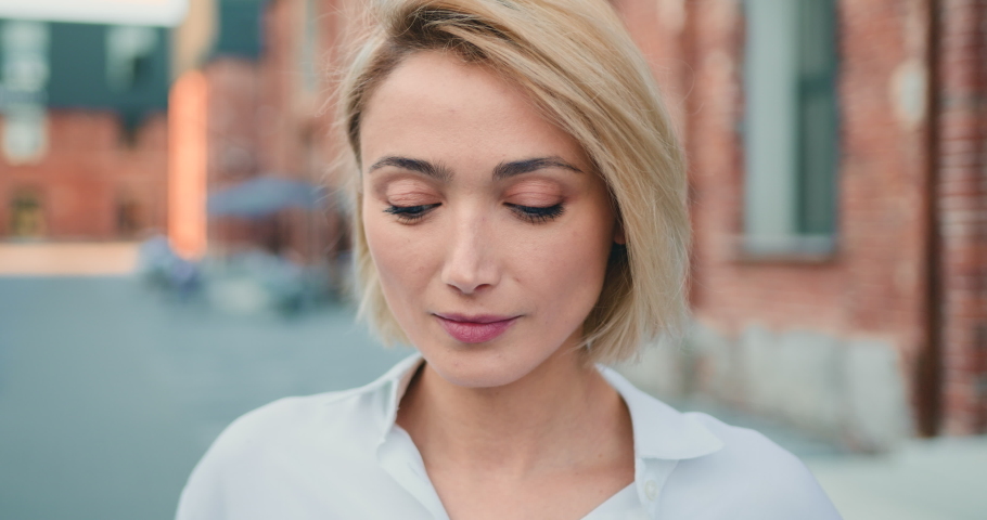 Close up portrait blond young attractive smile woman look at camera at city street. Outdoor portrait happy female girl.