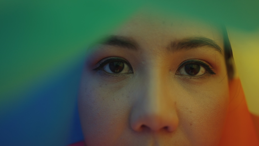Portrait young teen queer transgender asia people look at camera under colorful stripes flag. Closeup eye face cry sad hiding true self identity in gay LGBTQ LGBTQIA bisexual mental illness problem.  | Shutterstock HD Video #1091285957