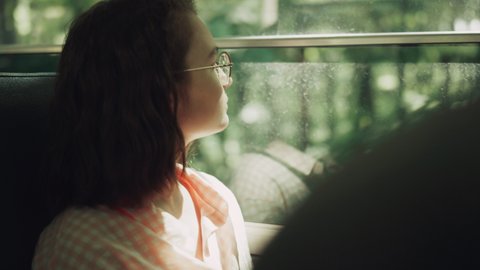 Pensive school girl sitting bus alone close up. Teen passenger brunette looking window on greenery. Thoughtful teenager watching nature outside on daily trip. Dreamy schoolgirl in glasses enjoy ride.