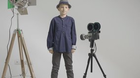 Child takes off his hat i front of video camera, spotlight reflector at studio