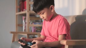 Asian boy playing a portable video game on the couch. A 6 year old kid enjoys gaming time.