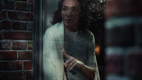Hispanic Female in Deep Depression, Runs her Finger across Rainy Window Glass and Thinking About Life Problems. Portrait of a Troubled Lonely Woman. Mental Health, Domestic Abuse concept