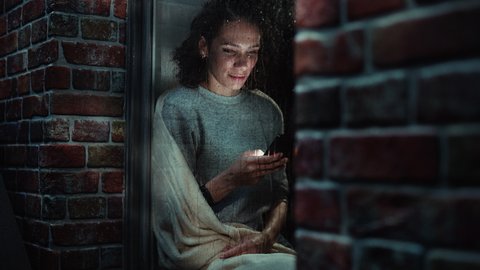 Sad Woman Sits at the Window at Night and Uses Smartphone, using Social Media App or Dating Online. Female Waiting for a Message from her Love Interest while it Rains Outside. Inside Apartment Window 